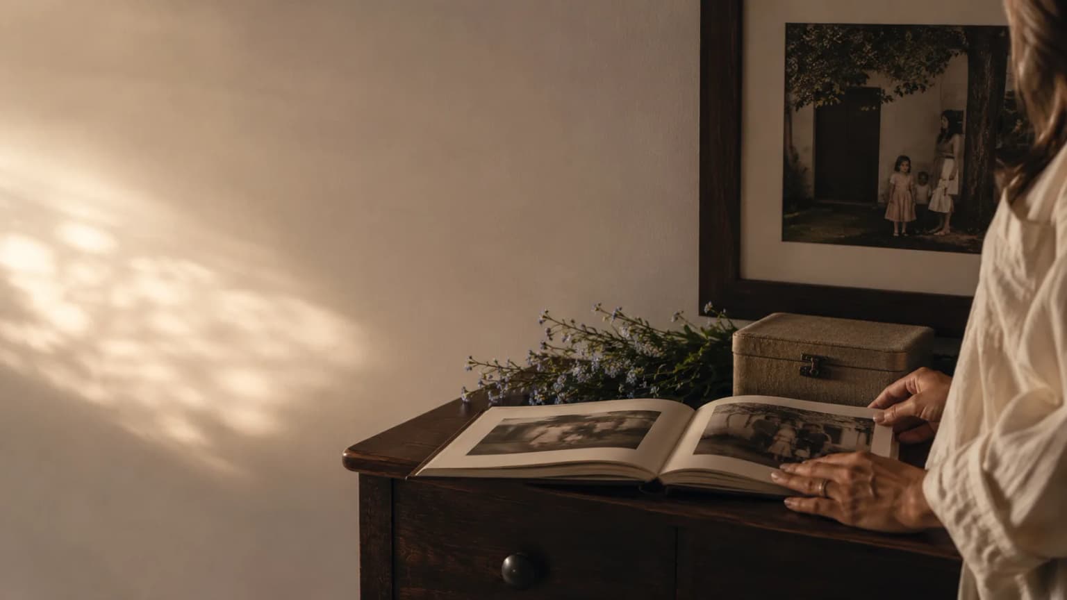 Mulher folheia um livro de memórias diante de um quadro de família.