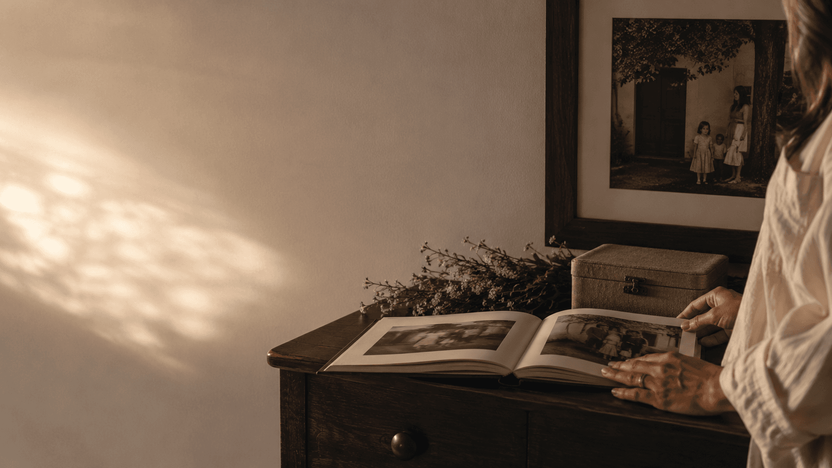 Mulher folheia um livro de memórias diante de um quadro de família.